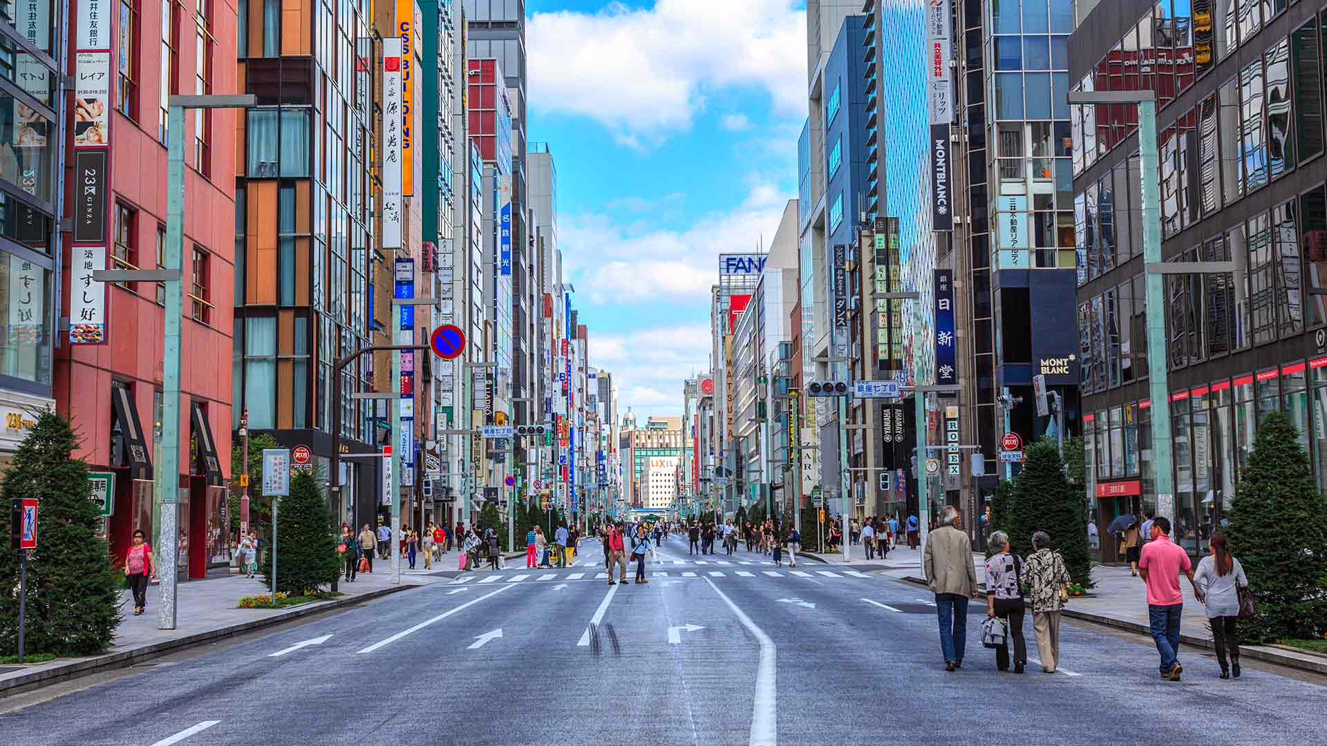 Busy urban street in Ginza, Tokyo, featuring shops, pedestrians, and vibrant city life under a bright blue sky.