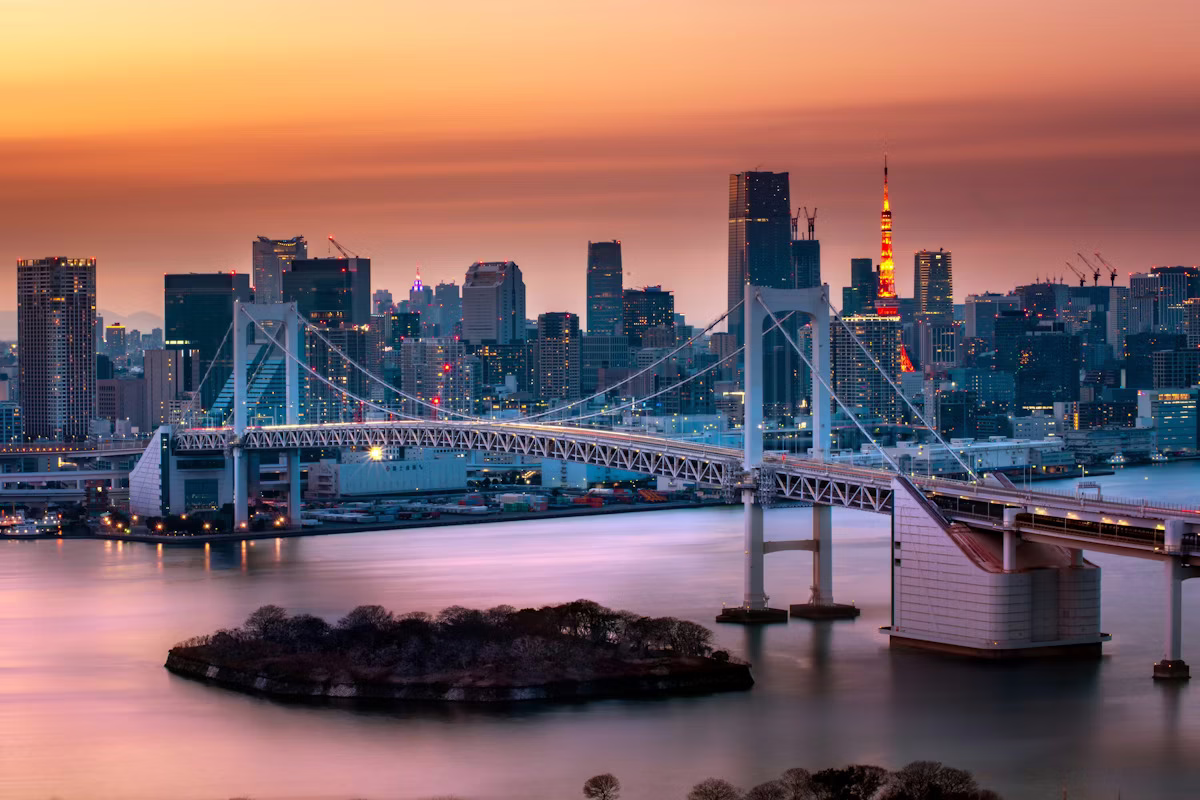 "Tokyo skyline at sunset, featuring Rainbow Bridge and Tokyo Tower illuminated against a colorful sky."
