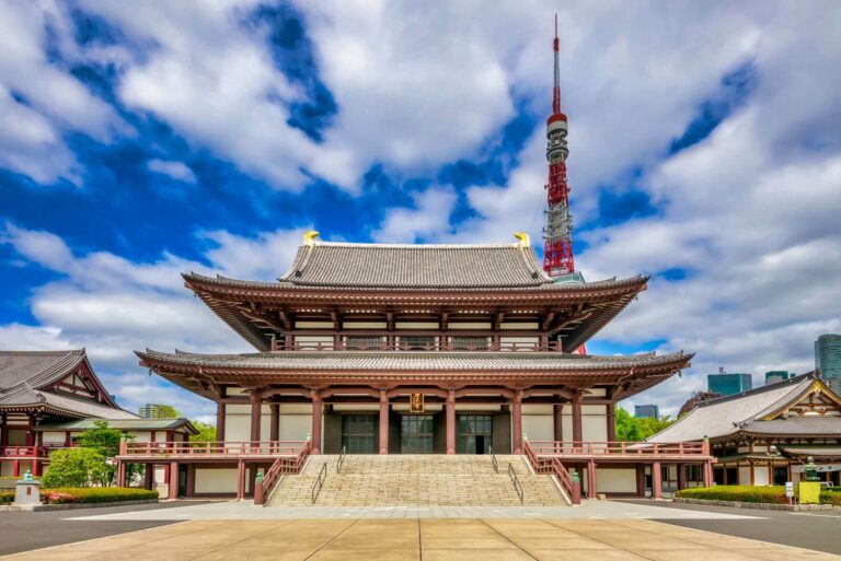 Traditional Japanese temple building at Shiba Park Tokyo with intricate architecture, juxtaposed against Tokyo Tower and a vibrant blue sky.