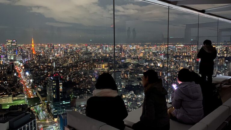 Evening view of Tokyo's skyline with illuminated skyscrapers and visitors enjoying the breathtaking cityscape from a high vantage point.