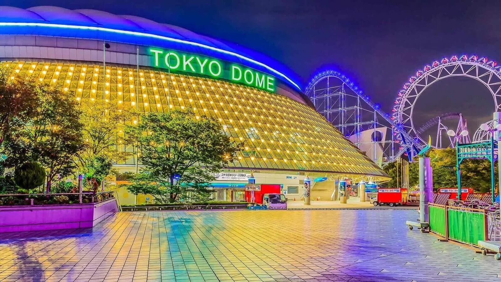 Vibrant Tokyo Dome illuminated at night with a colorful amusement park in the background, showcasing a lively urban atmosphere.