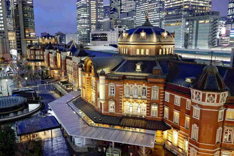 Illuminated Tokyo station at dusk, blending historic architecture with modern cityscape, a hub of vibrant urban life.