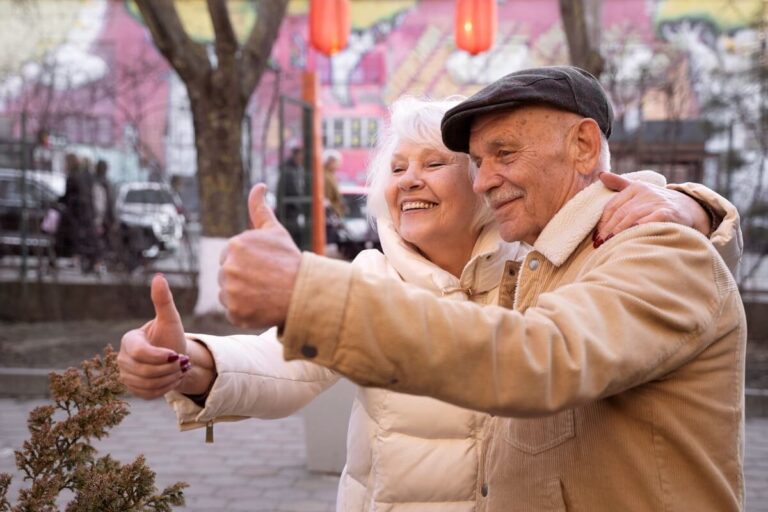 Happy elderly couple enjoying a moment together, both giving thumbs up in a vibrant outdoor setting showcasing joy and companionship.