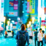 Bustling city scene featuring pedestrians navigating vibrant streets adorned with neon signs and illuminated lanterns.