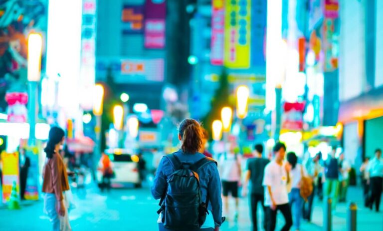 Bustling city scene featuring pedestrians navigating vibrant streets adorned with neon signs and illuminated lanterns.