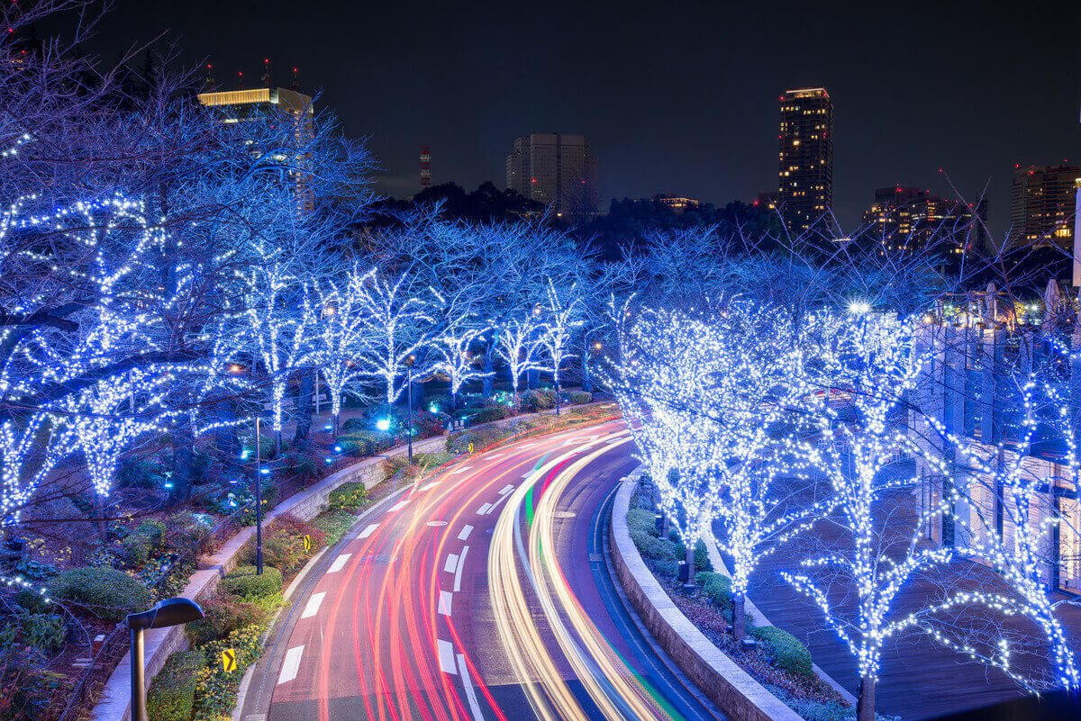 Enchanting winter night scene featuring vibrant blue lights on trees lining a curving road, creating a festive atmosphere.