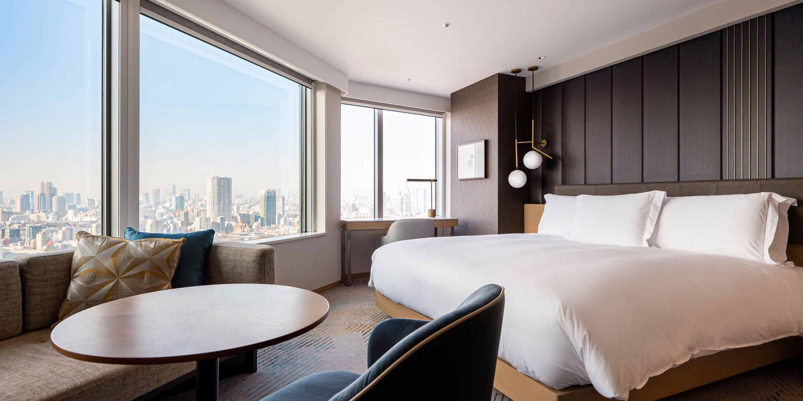 Stylish hotel room featuring a sleek bed and a cozy seating area, with panoramic city views through large windows.
