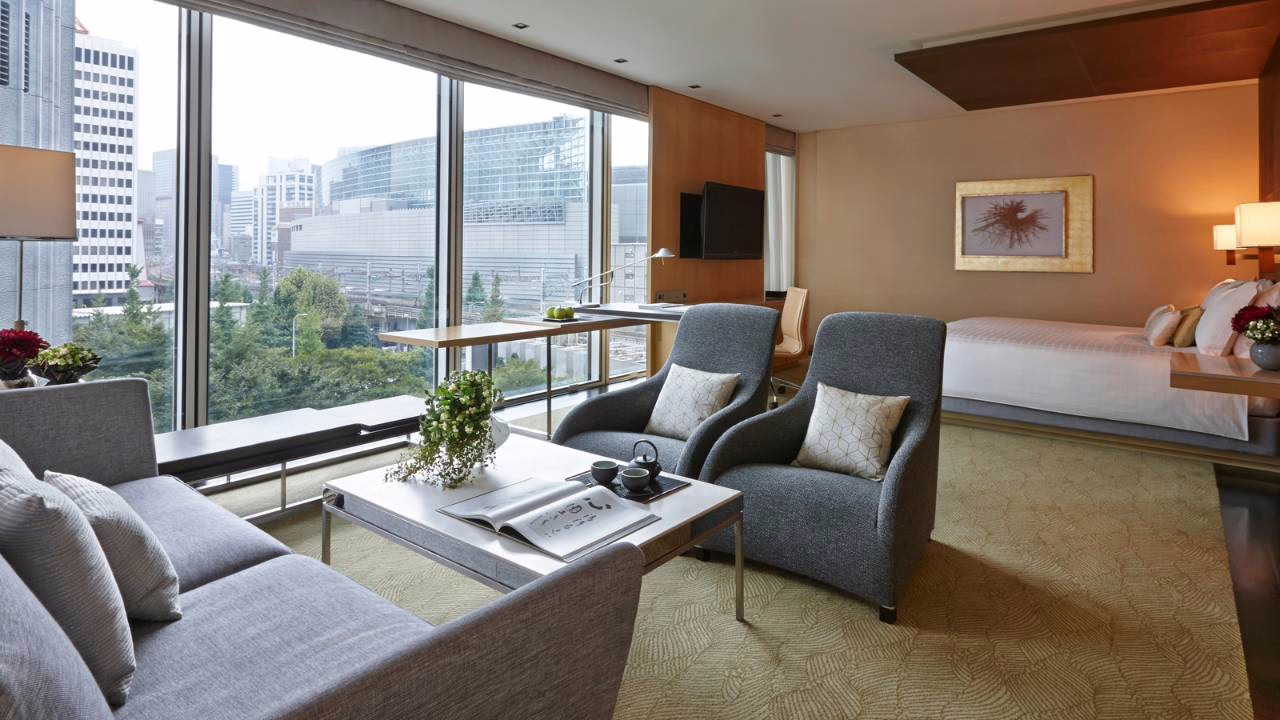 Modern hotel room featuring stylish seating, a cozy atmosphere, and stunning city views through large windows.