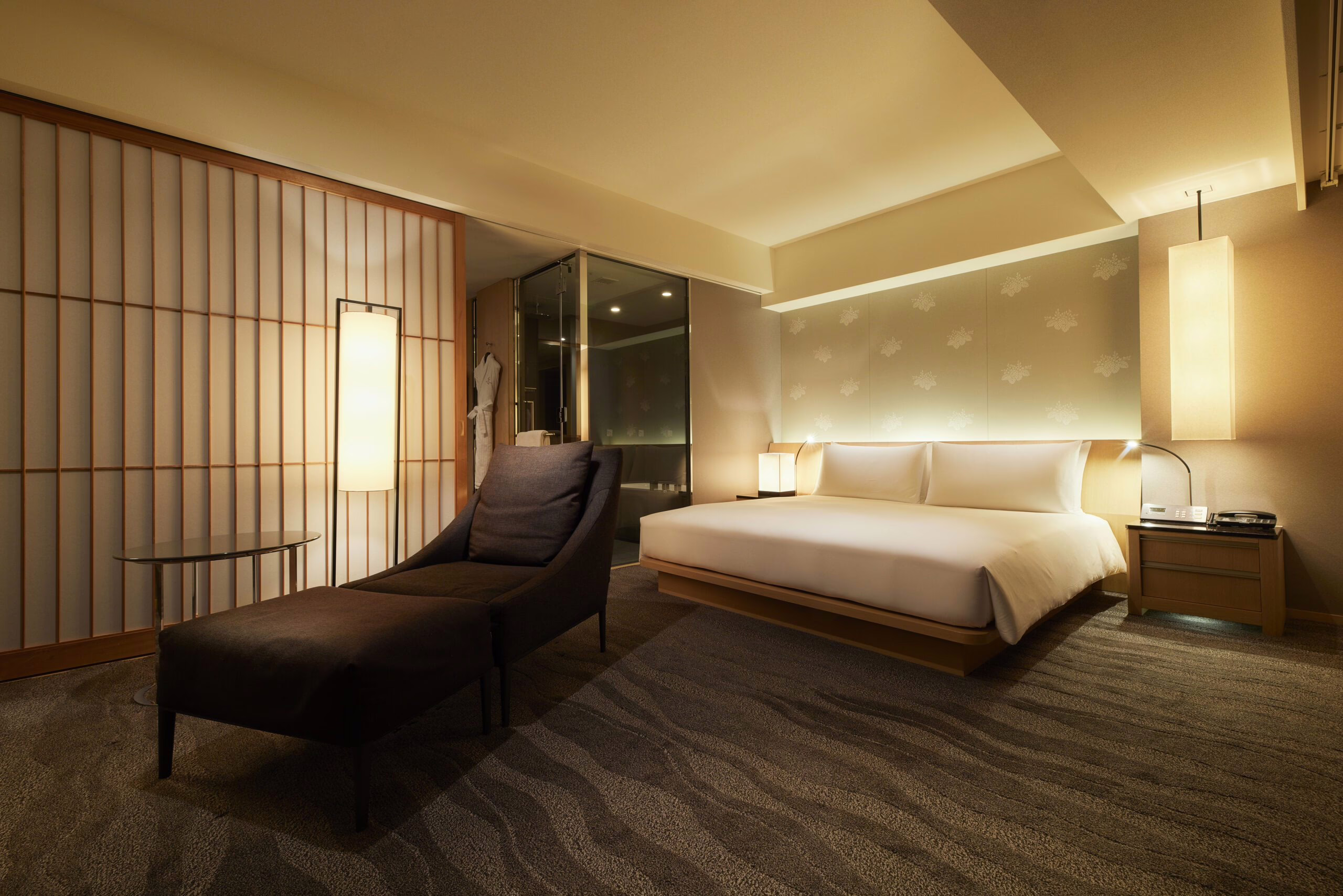 Luxurious hotel room with minimalist design, featuring a king-size bed, cozy chaise lounge, and soft ambient lighting.