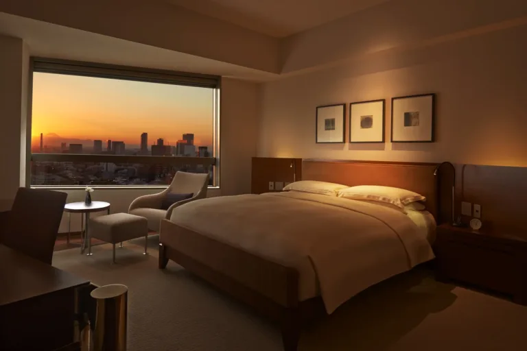 Modern hotel room featuring a cozy bed, sleek workspace, and a stunning sunset view over the cityscape.
