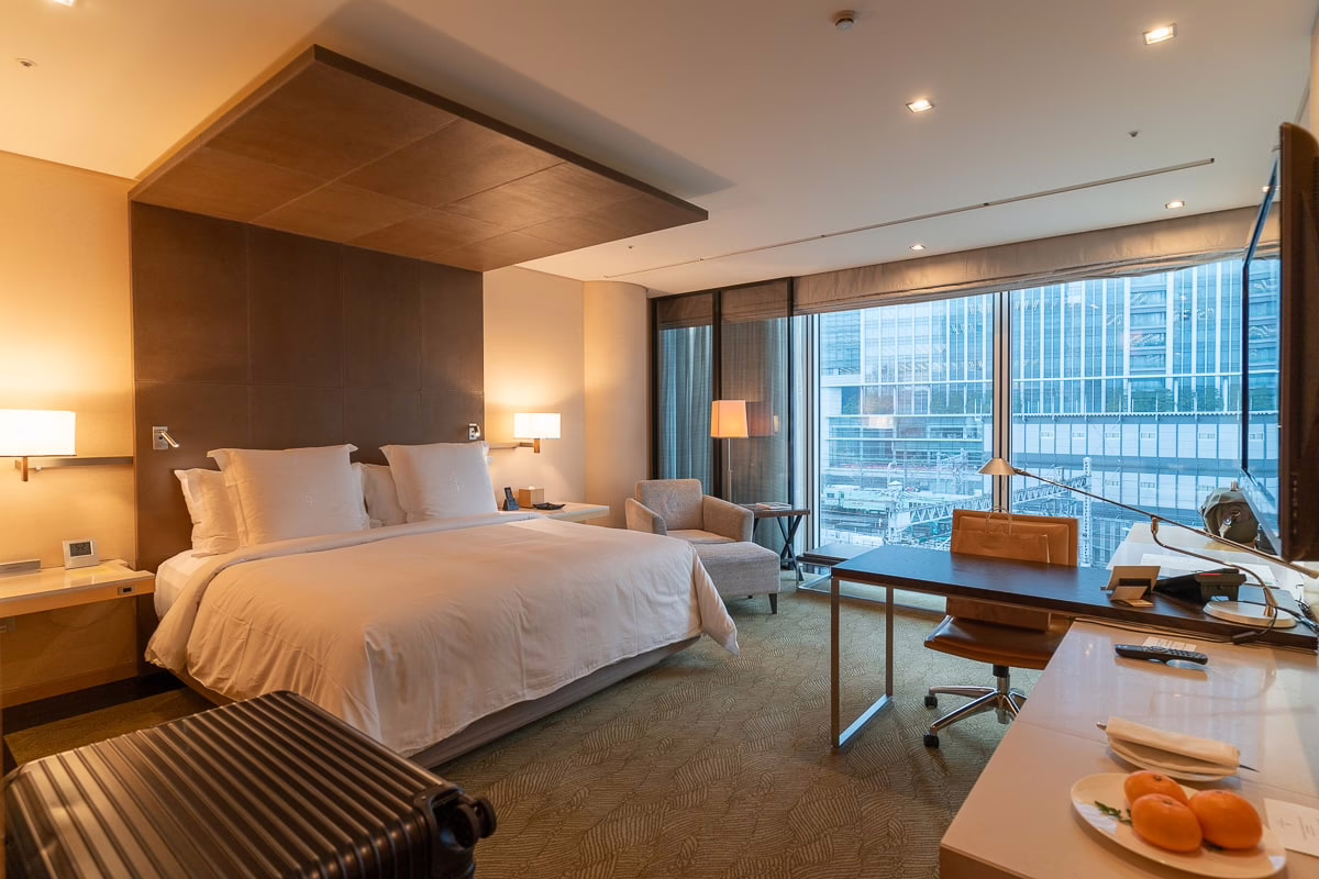 Luxurious hotel room featuring a king-sized bed, modern furnishings, and a large window with a city view.