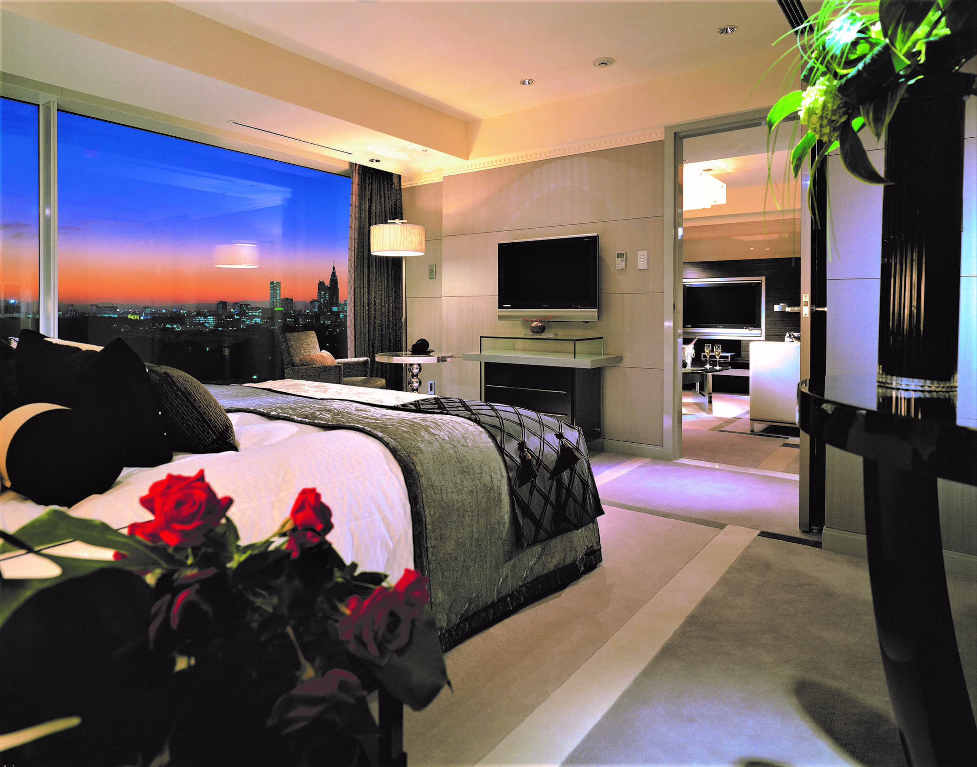 Luxurious hotel bedroom with a stunning city view at sunset, featuring elegant decor and cozy ambiance.