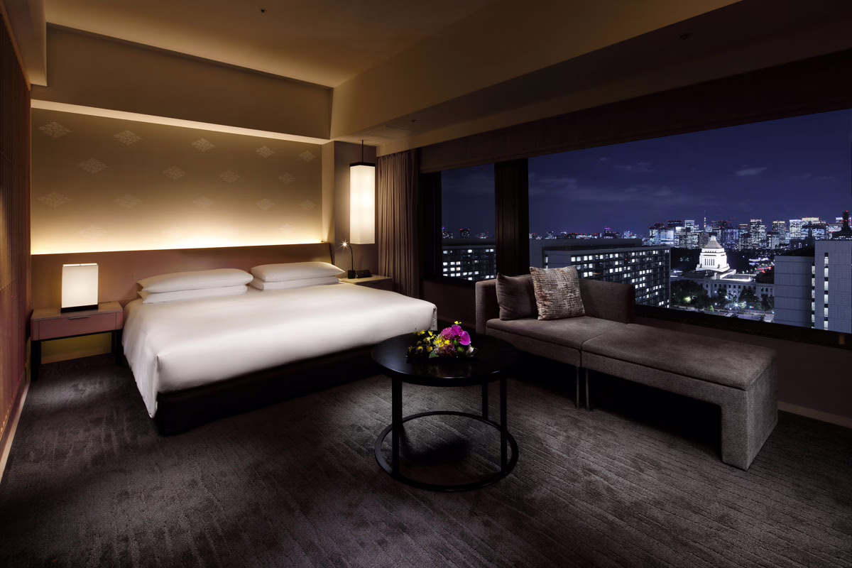 Elegant hotel room featuring a king-size bed and a cozy seating area with stunning city views at night.