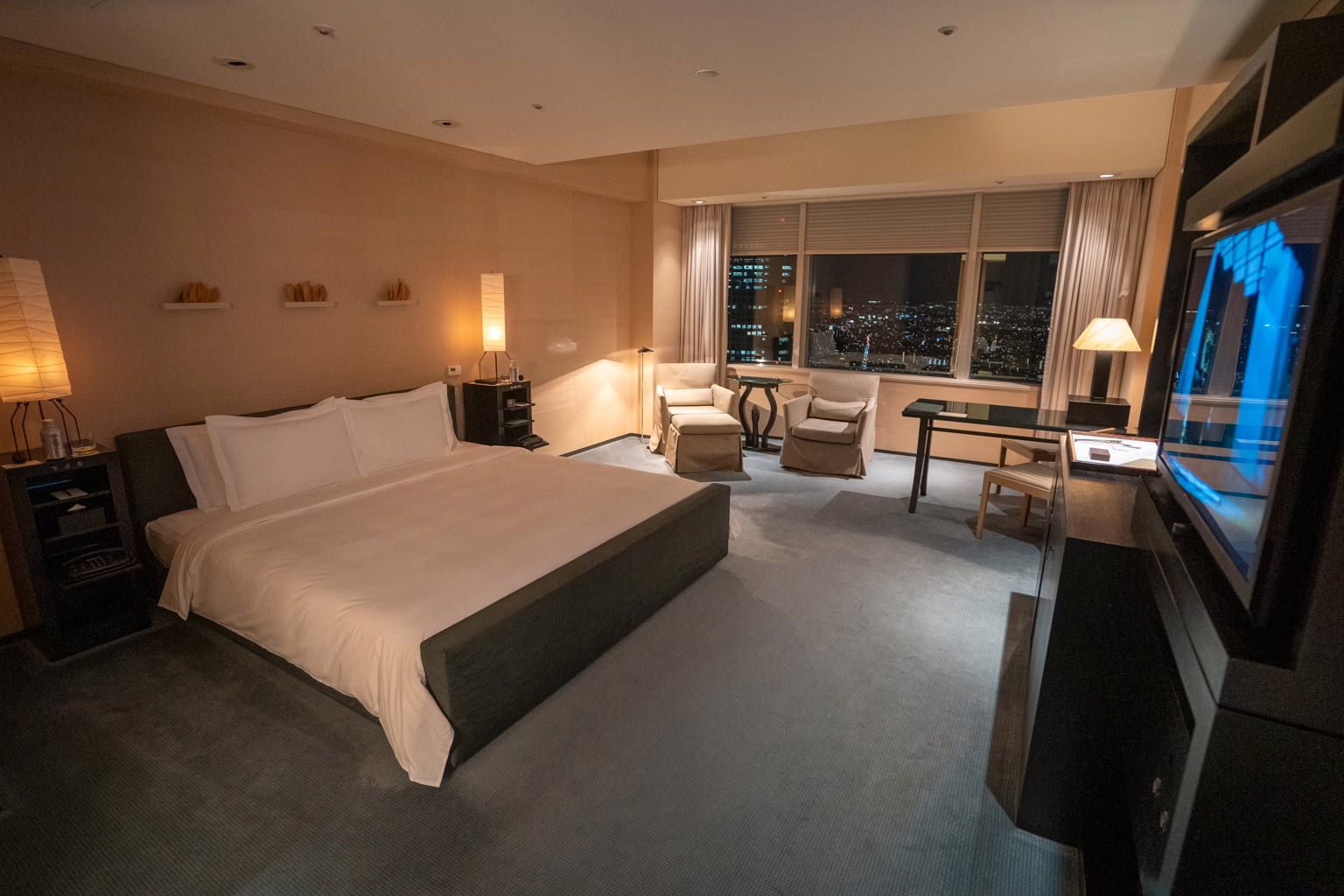 Luxurious hotel room featuring a king-sized bed, stylish decor, and stunning city views at night.