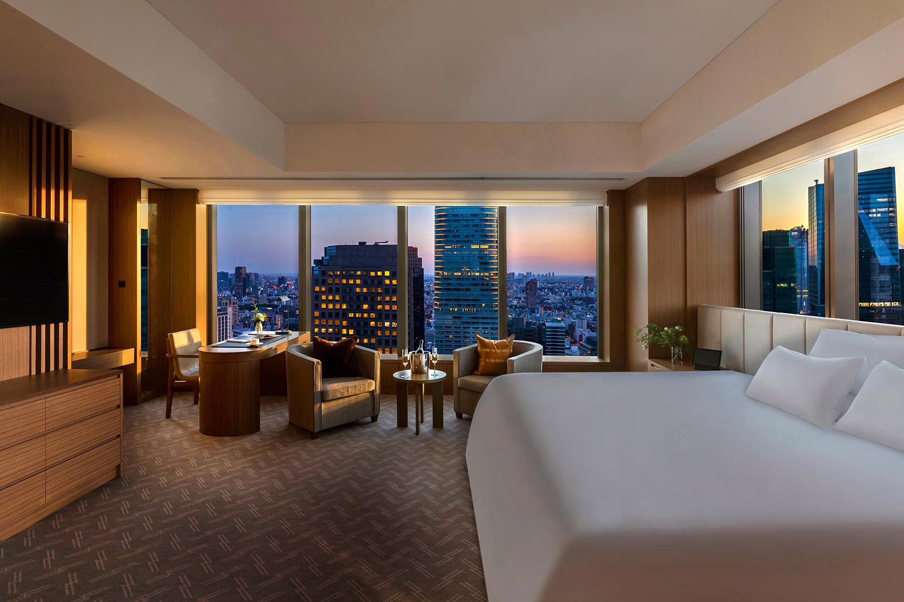 Luxurious hotel suite with city skyline views at sunset, showcasing modern decor and a cozy sitting area.
