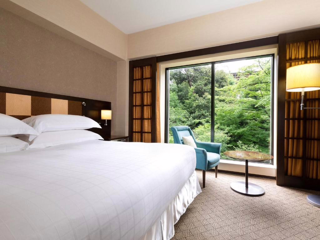 Modern hotel room featuring a king-size bed, cozy seating area, and large window overlooking lush greenery.