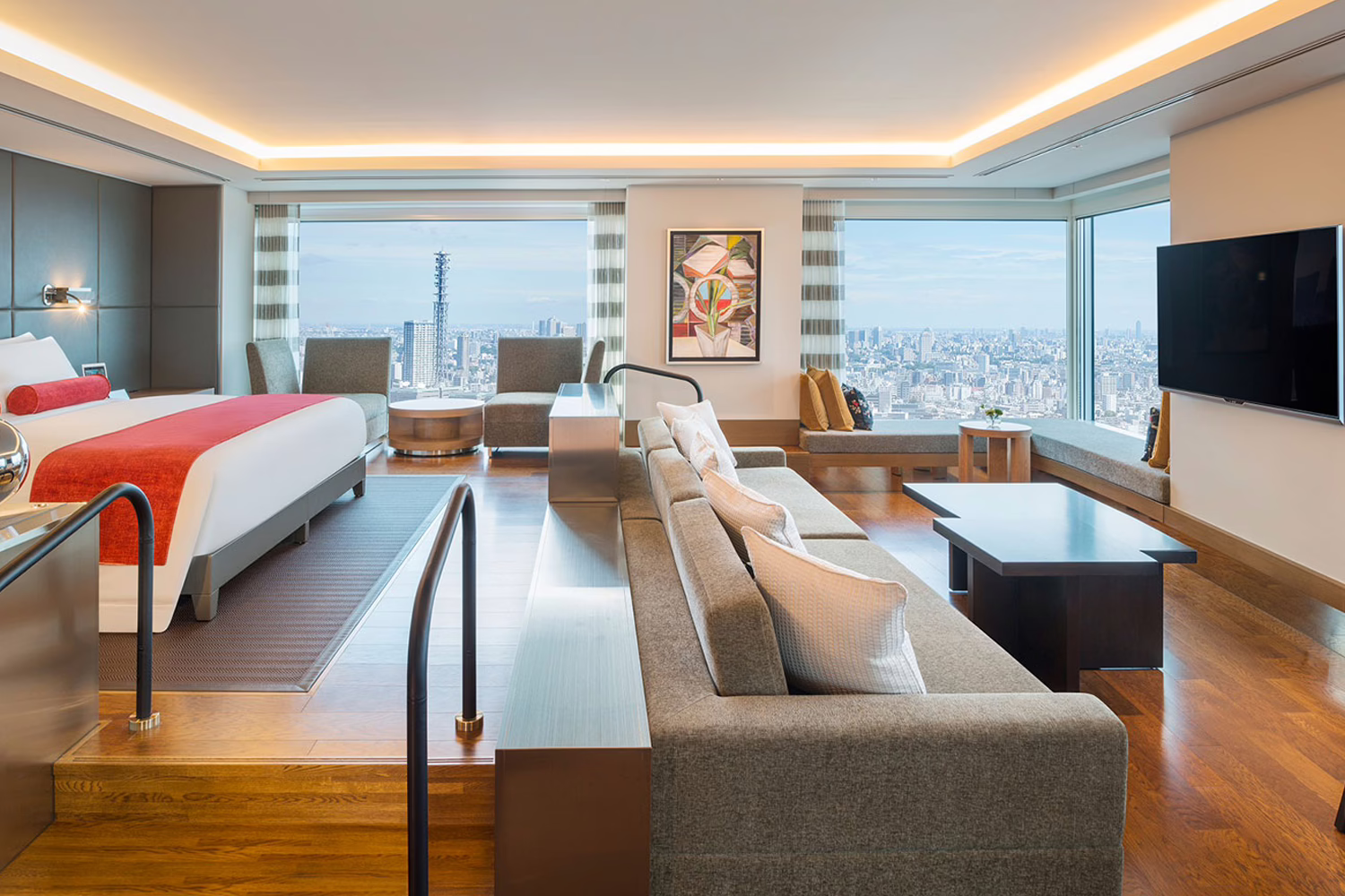 Modern hotel suite with panoramic city views, featuring a cozy bedroom, stylish seating area, and contemporary decor.