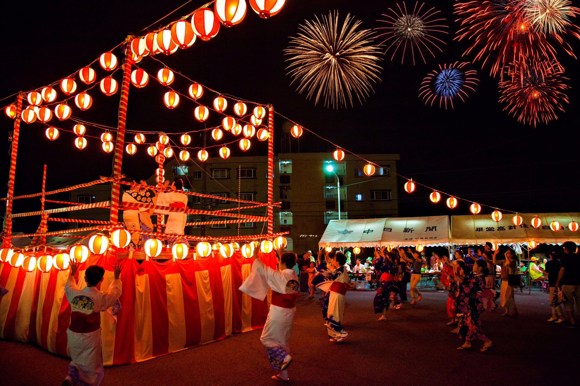 A vibrant summer festival scene with traditional dancers in yukatas celebrating under glowing lanterns and fireworks.