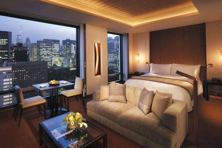 Luxurious hotel room featuring two beds and a stunning view of the city skyline and lush greenery outside.