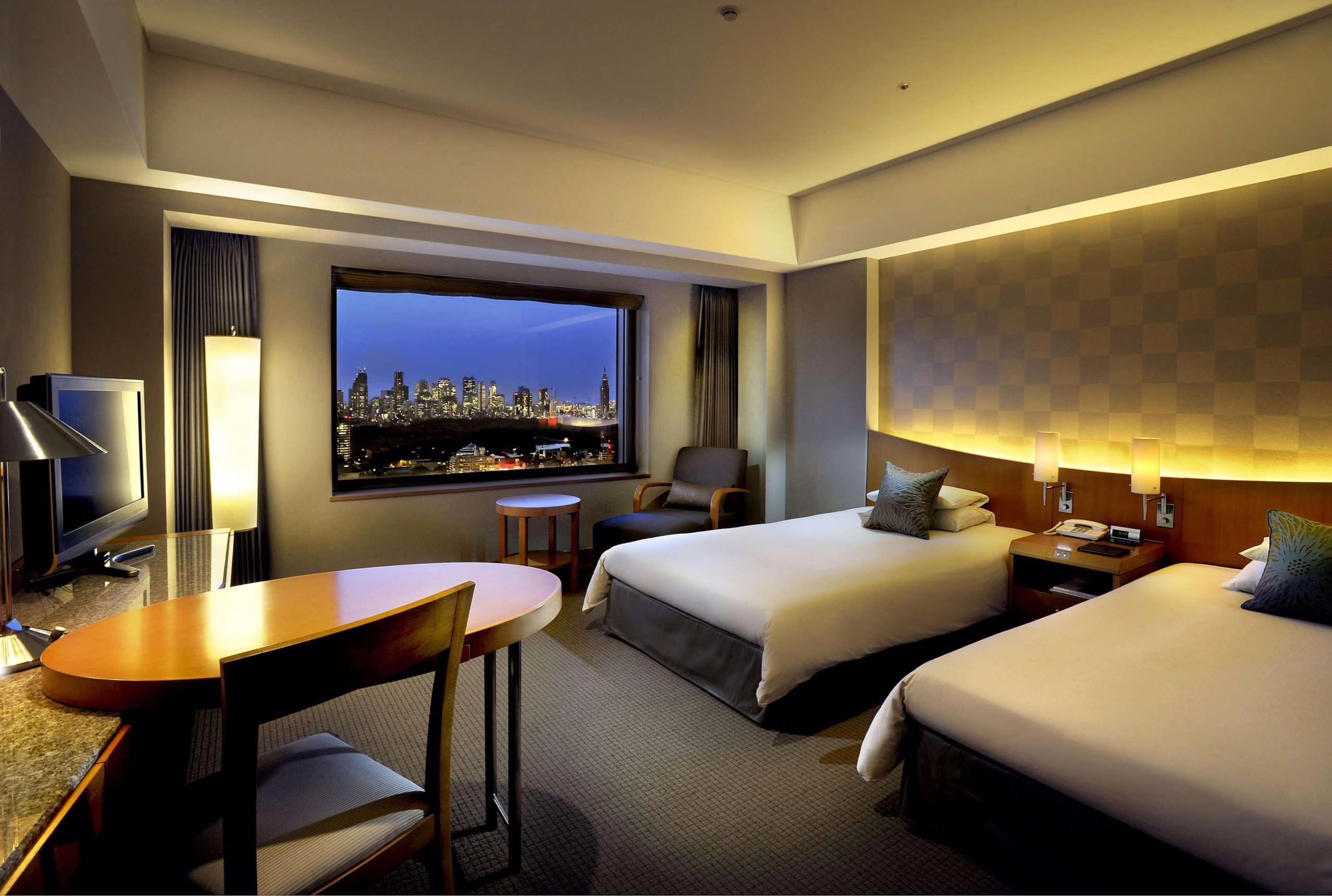 Elegant hotel room with two beds and a stunning city skyline view at dusk, offering a cozy and inviting atmosphere.