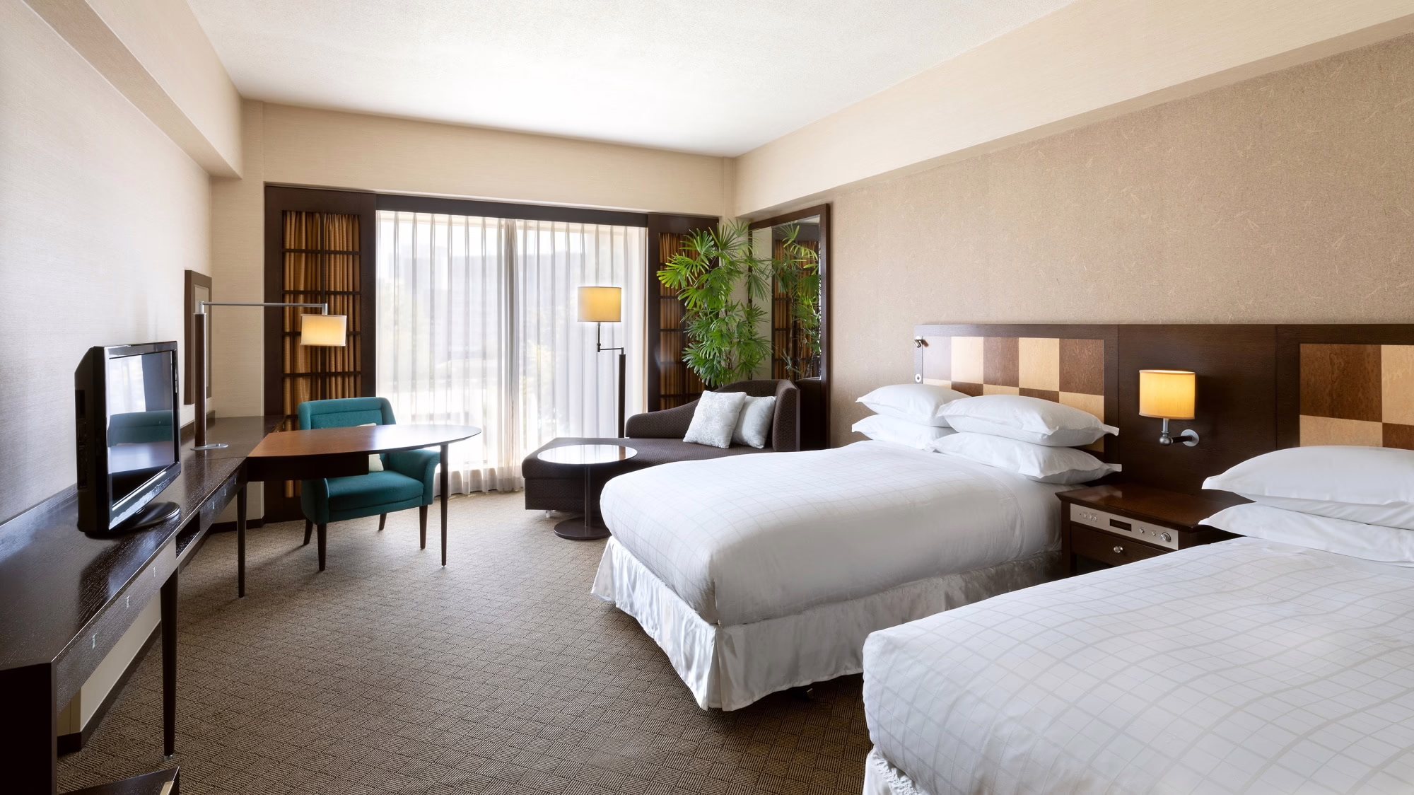 Modern hotel room featuring two twin beds, a comfortable seating area, and large windows with natural light.