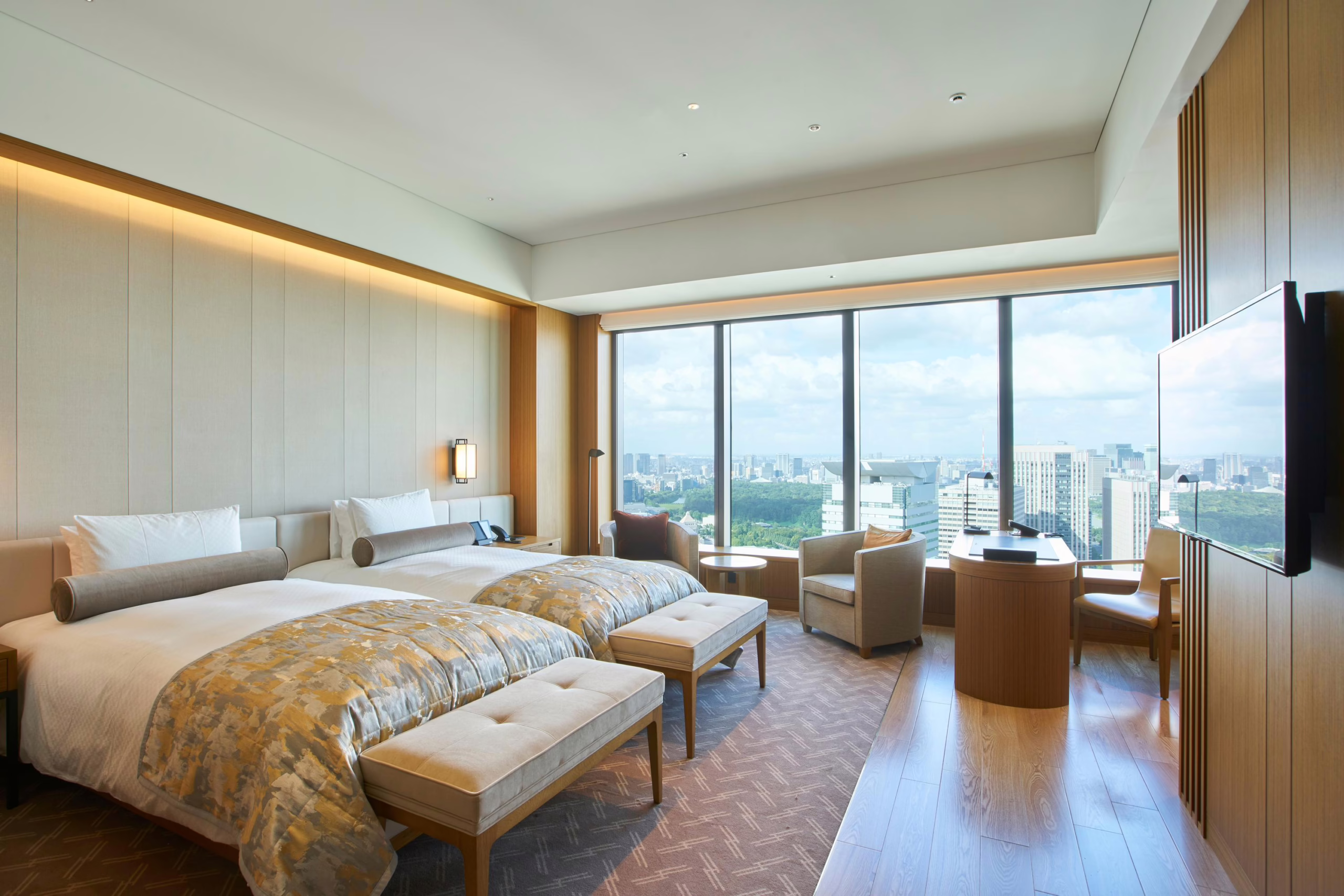 Stylish hotel room with twin beds, modern furnishings, and stunning city views through large windows.