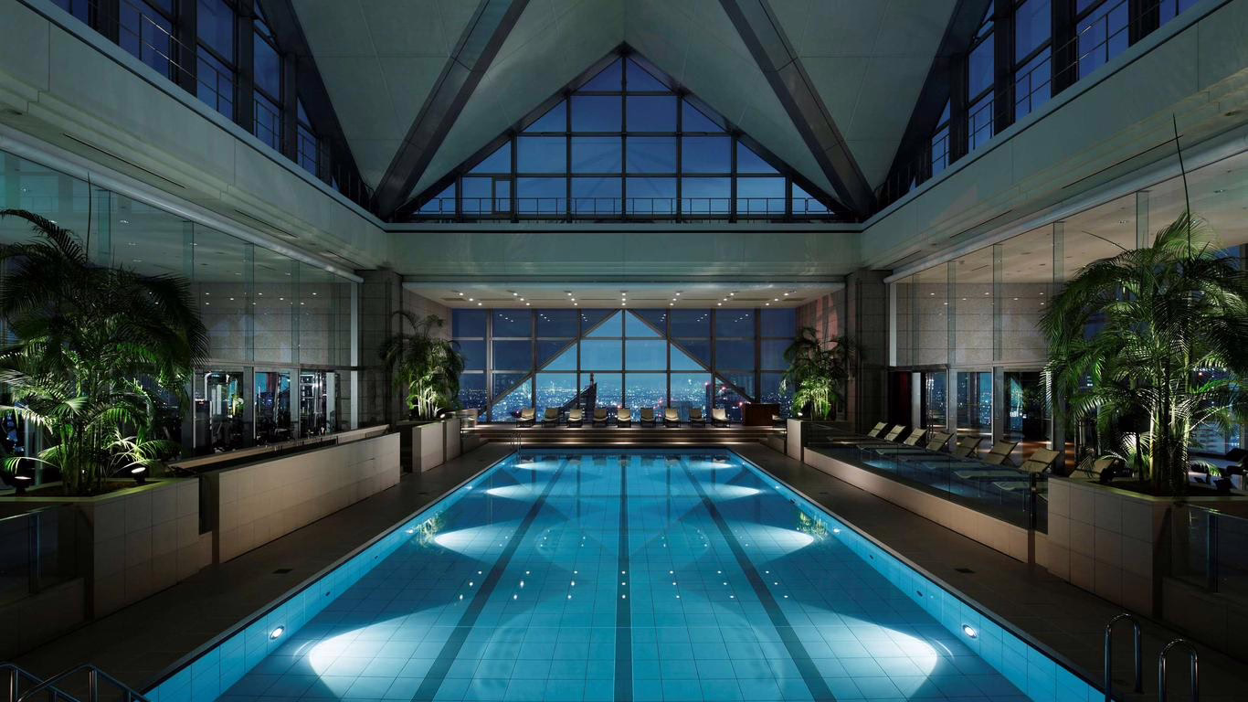 Luxurious indoor swimming pool featured in a high-rise with city skyline views illuminated at night, creating a serene atmosphere.