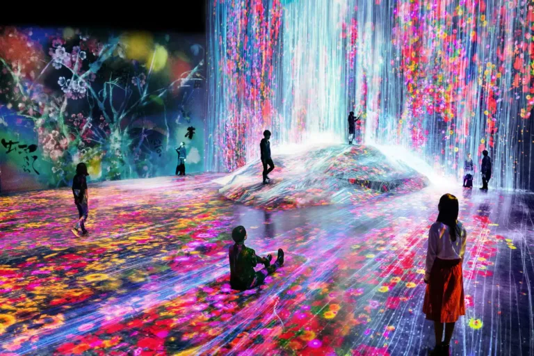 Colorful digital art installation with visitors exploring a vibrant landscape of flowers and cascading light effects.