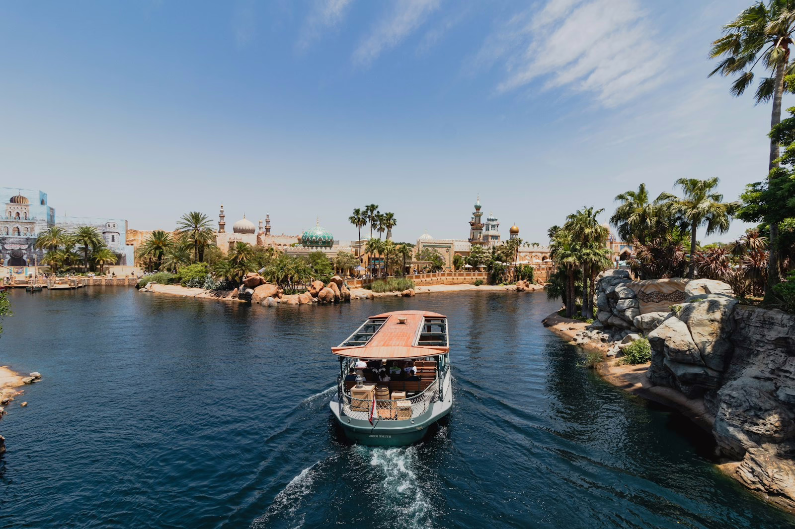 Scenic view of a boat cruising through serene waters surrounded by lush palm trees and exotic architecture.