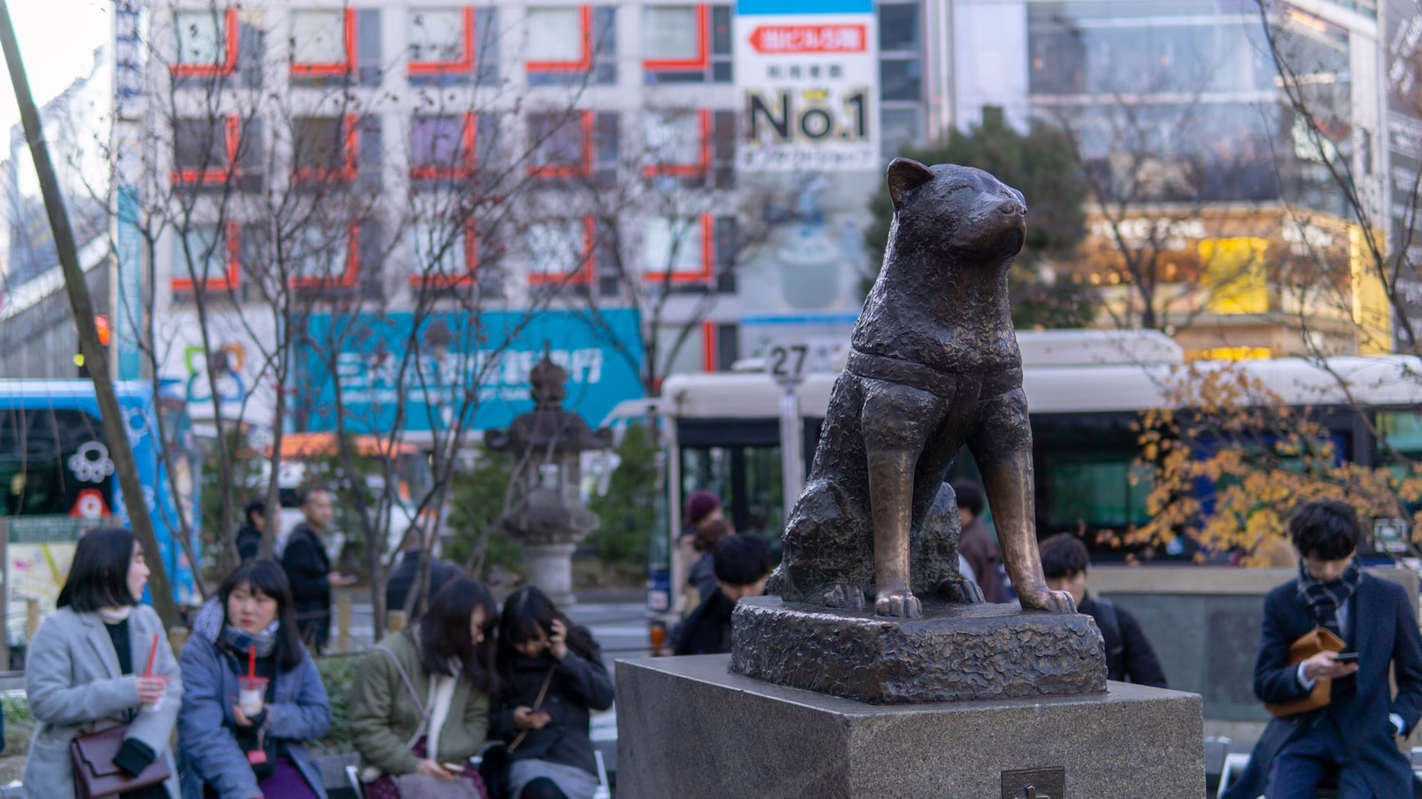 Hachiko statue honoring loyalty stands in a bustling Tokyo square, surrounded by people relaxing and exploring the area.