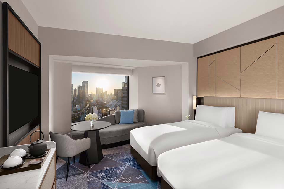 Modern hotel room with city views, featuring twin beds, minimalist decor, and a cozy seating area for relaxation.