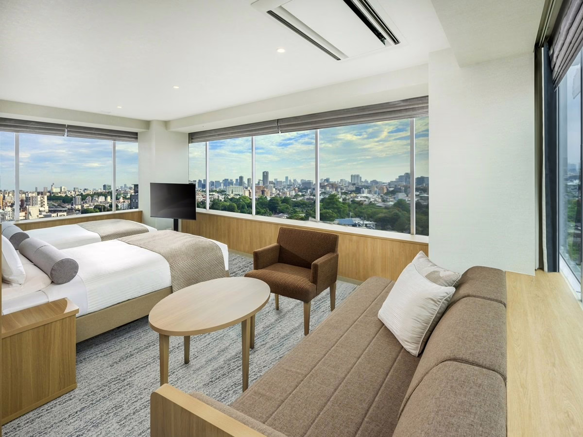 Stylish hotel room featuring twin beds, modern furnishings, and large windows with a panoramic city view.