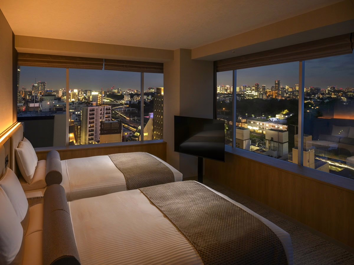 Modern hotel room with two beds, showcasing a stunning city skyline at night through large windows, inviting relaxation.