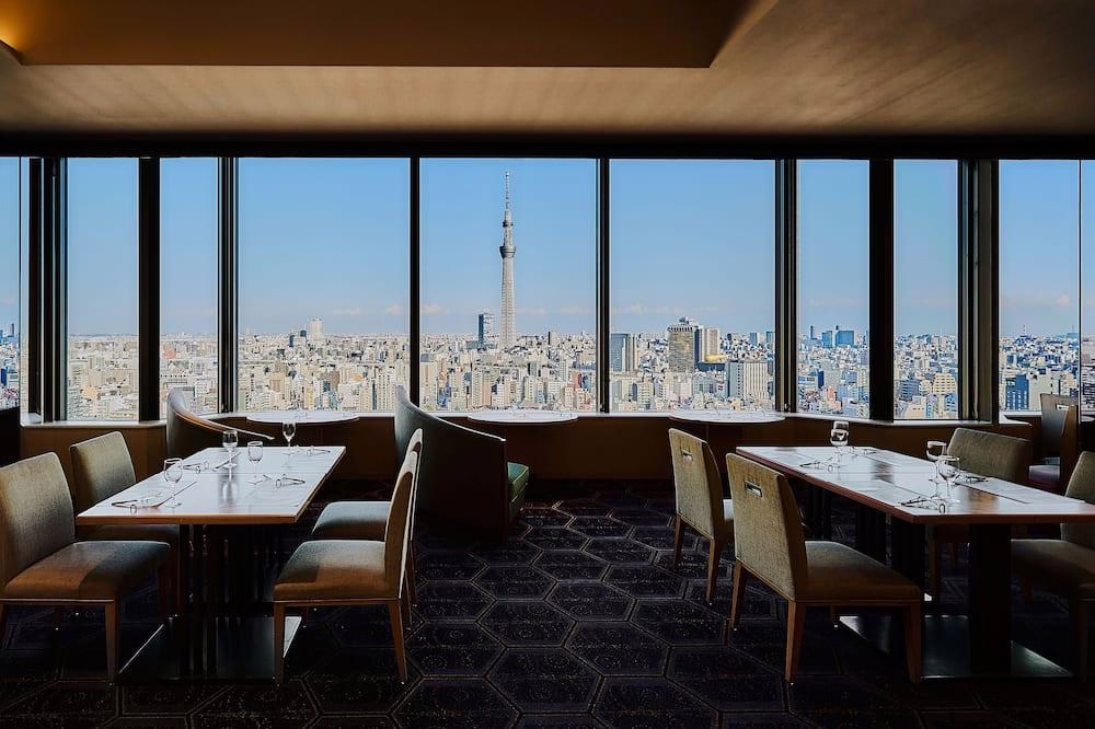 Modern restaurant interior with tables overlooking Tokyo skyline and Tokyo Skytree, offering a stunning dining experience.