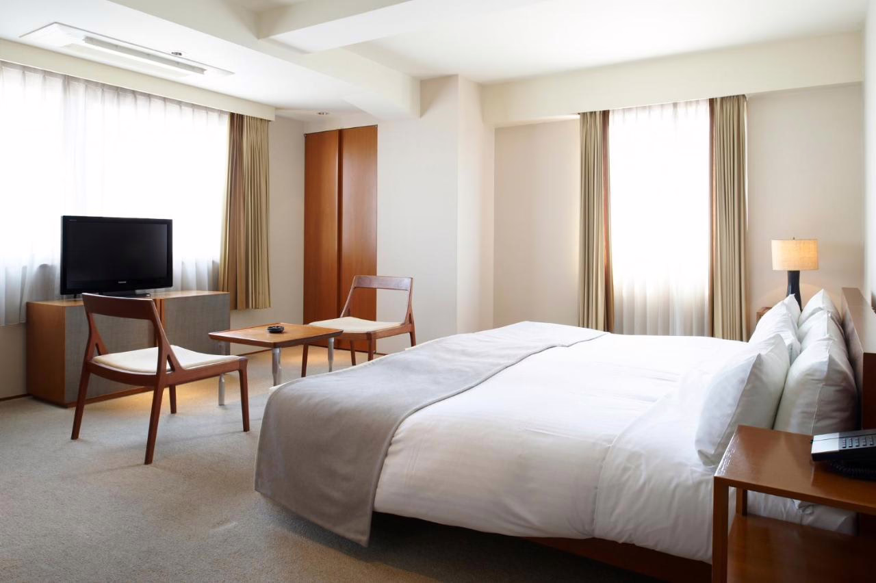 Modern hotel room featuring a cozy queen bed, wooden furnishings, and large windows for natural light. Perfect for relaxation.