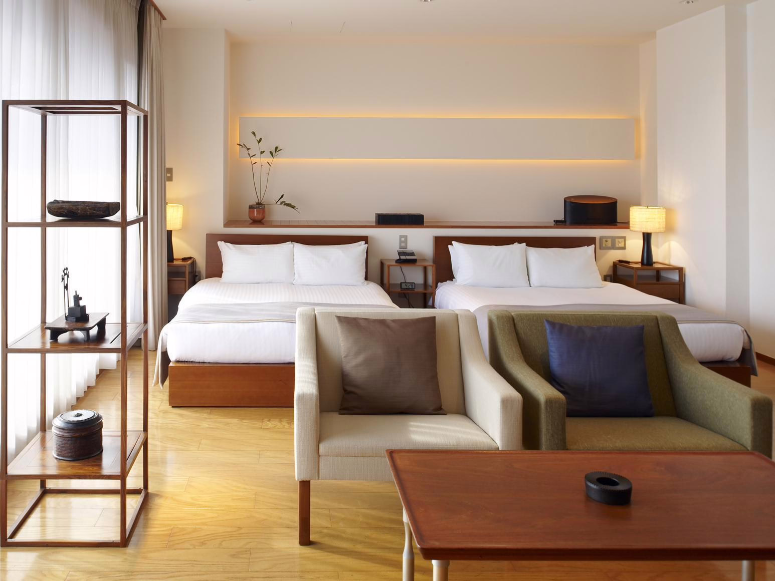 Modern hotel room featuring two beds, minimalistic decor, and cozy seating, perfect for restful stays and relaxation.