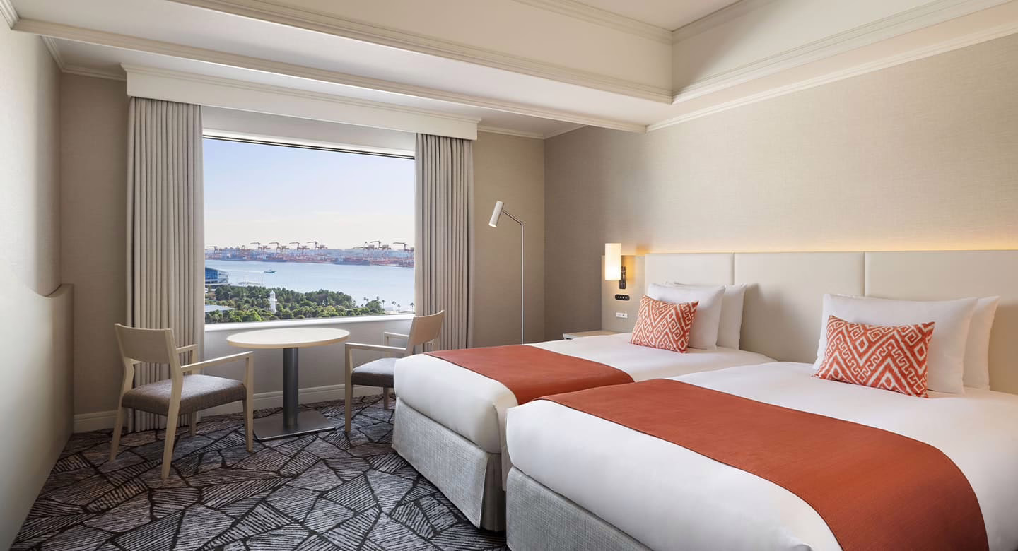 Spacious hotel room featuring twin beds, a cozy seating area, and a stunning view of the waterfront skyline.