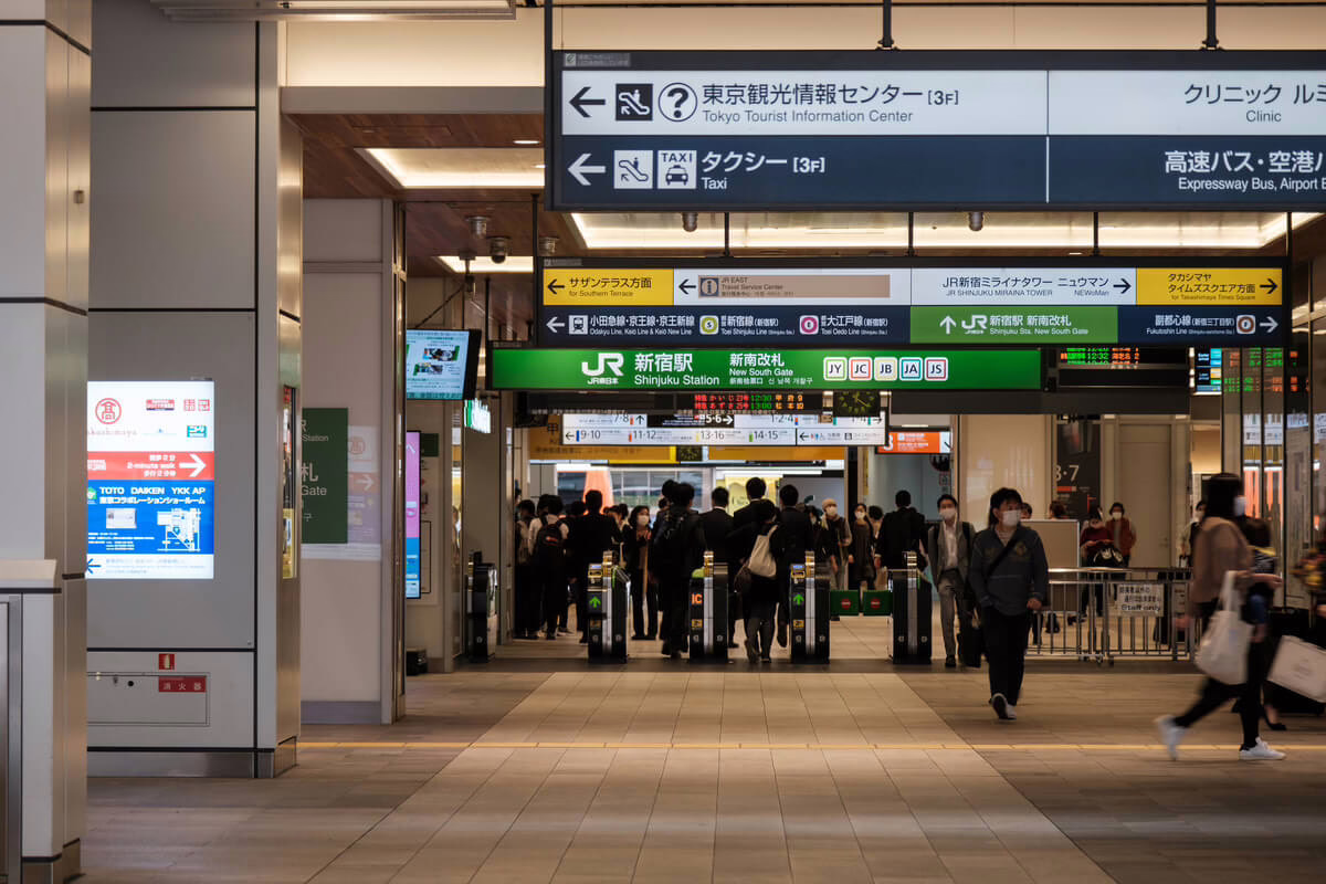 Crowded Shinjuku Station entrance with directional signs for taxis and tourist information, highlighting Tokyo's transit hub.