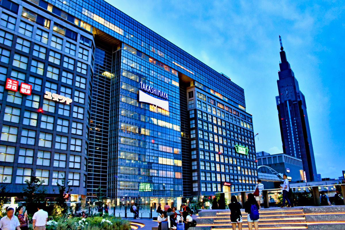 Modern Takashimaya department store in bustling urban setting, showcasing evening lights and lively street activity.