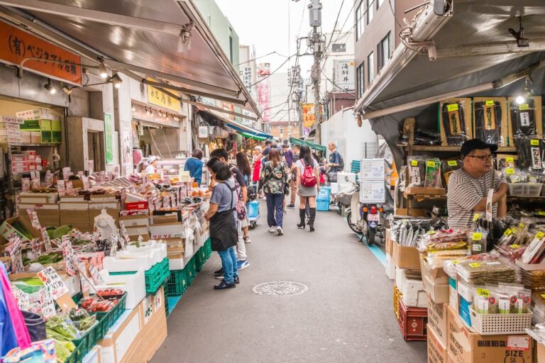 Bustling street market in Japan featuring vendors selling fresh produce and local goods amid lively shopping activity.