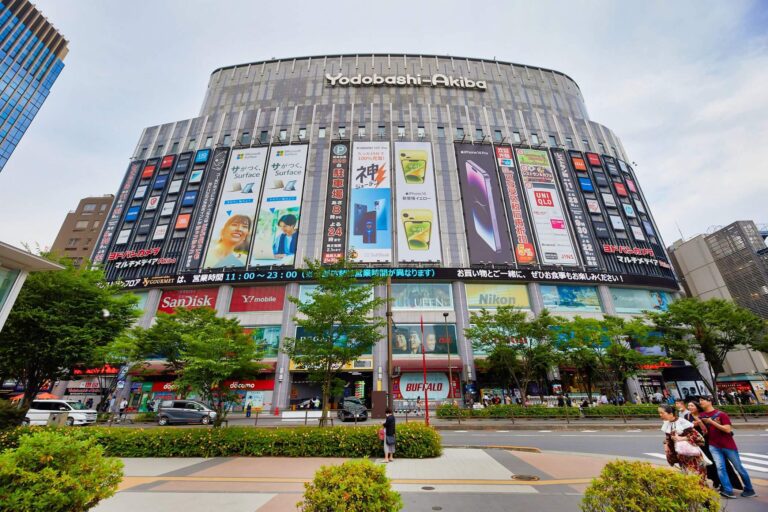 Yodobashi-Akiba, a bustling electronics store in Akihabara, showcases vibrant advertisements and diverse shoppers outside.
