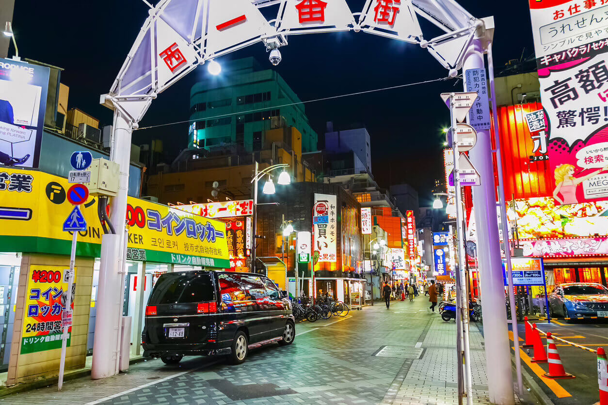 Vibrant nightlife in a bustling Tokyo street, illuminated by neon signs and filled with people and vehicles.